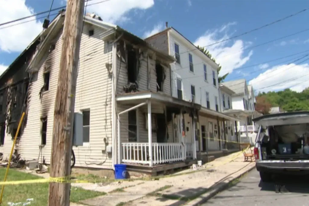 Exterior of a house partially damaged by fire, with yellow caution tape blocking off the area.