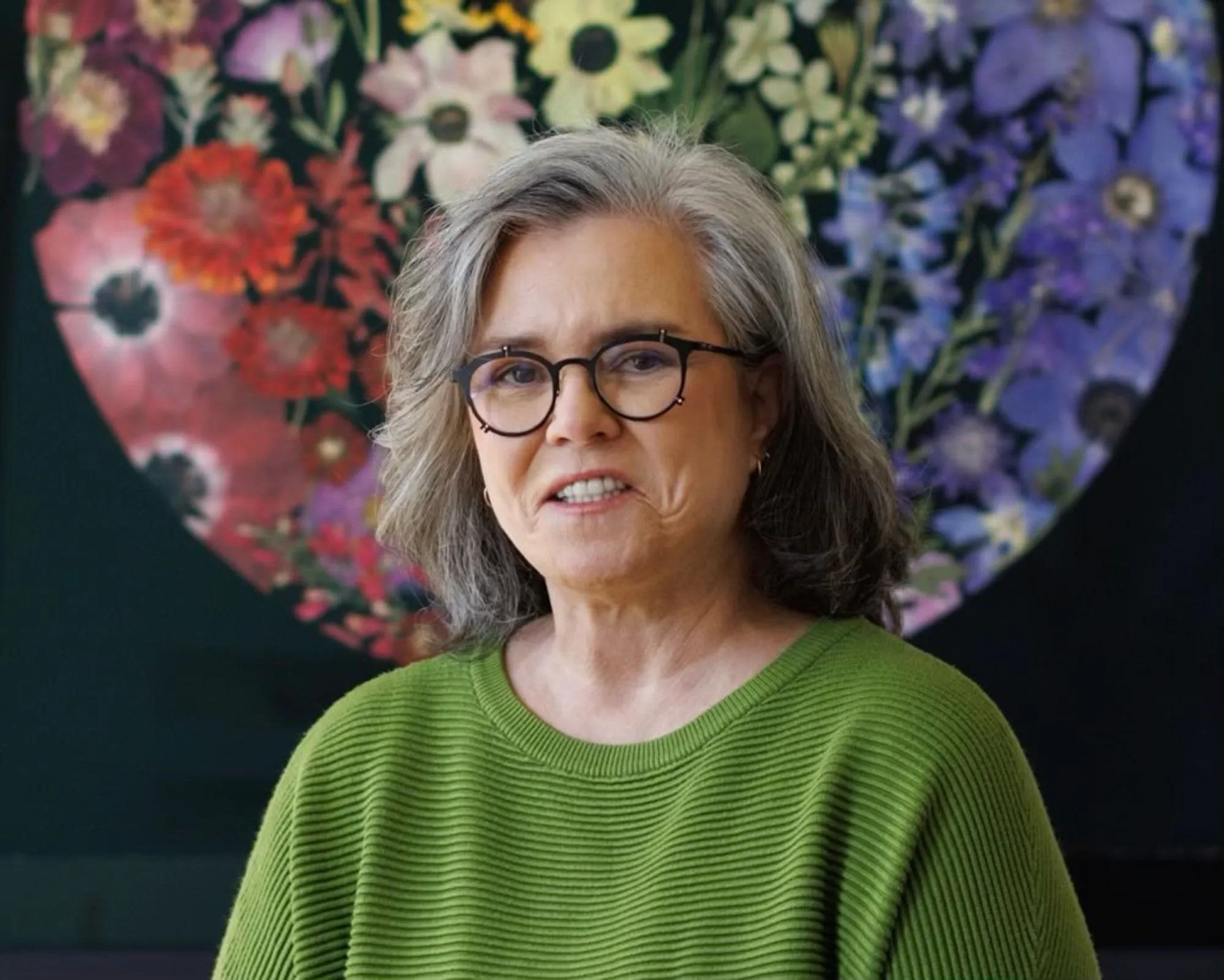 Rosie O'Donnell in a green top with a floral background.