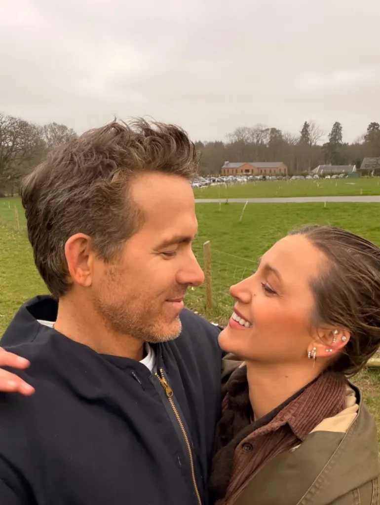 Ryan Reynolds and Blake Lively smiling at each other outdoors.