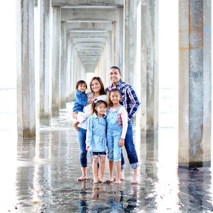 Maya Millete with her husband and three children standing barefoot under a pier.