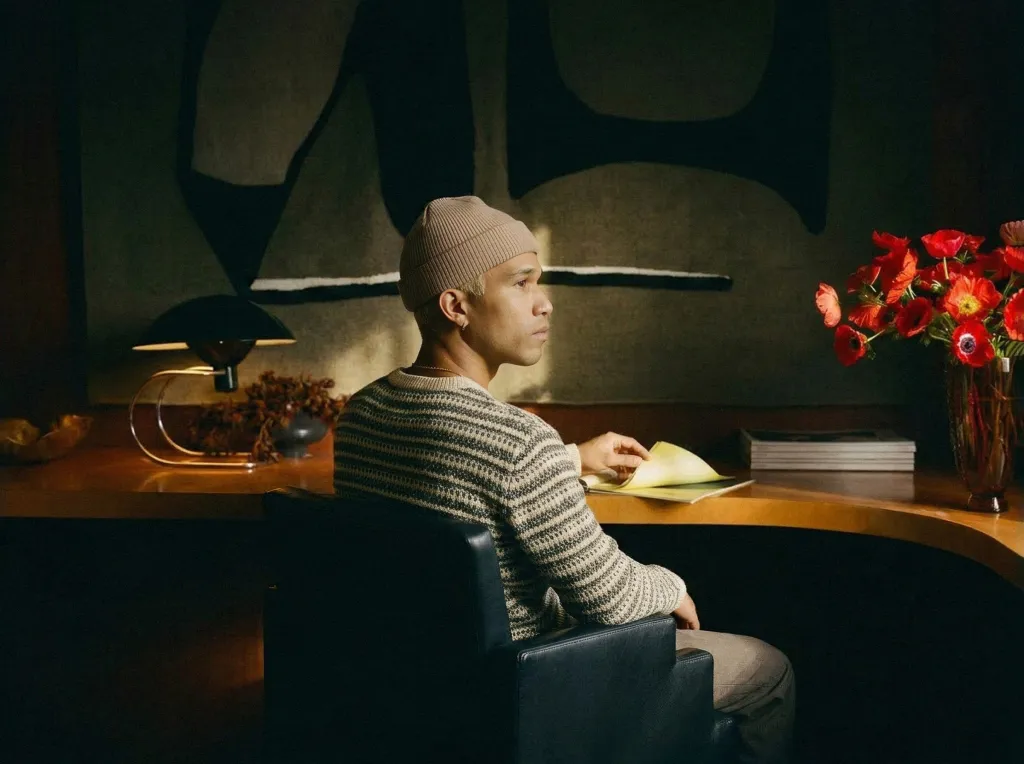 A person wearing a beanie and sweater sits at a curved desk, reading from a document.