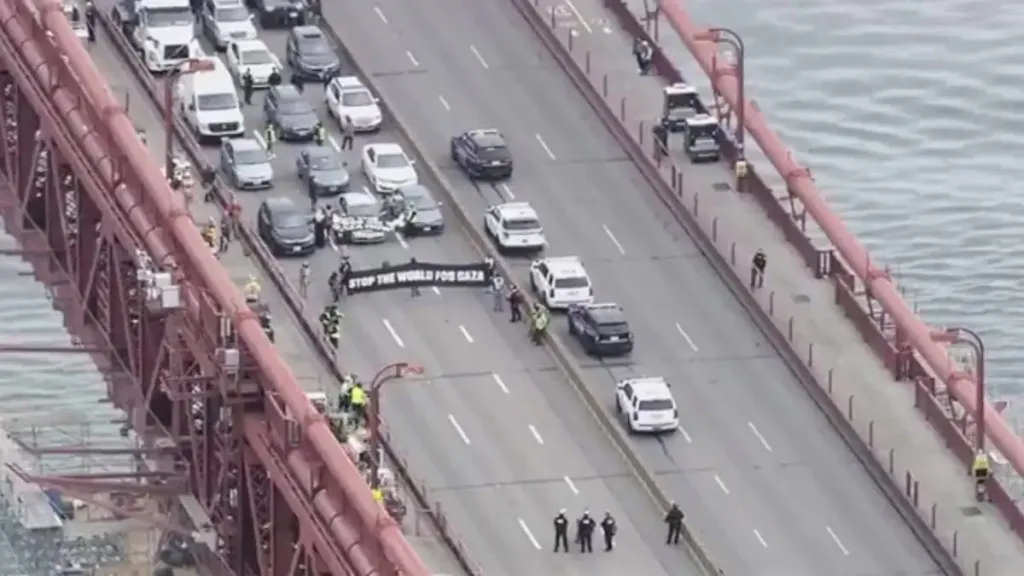 Protesters holding a banner across a road on the Golden Gate Bridge, blocking traffic.