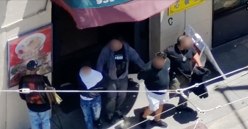 Two police officers escort three suspects from a building.