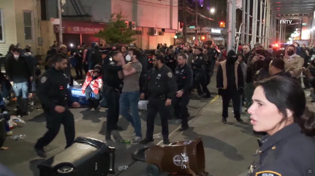 Police officers dragging a man from Wyckoff Hospital while protesters gather outside.