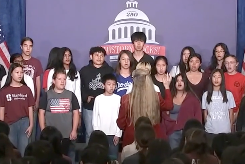 A group of middle and high school students sings on stage in front of a banner that reads 