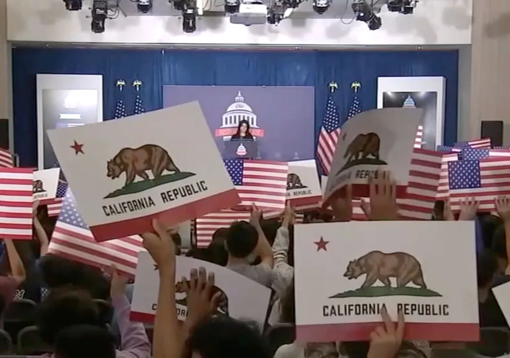 School assembly with students holding California Republic and American flags.