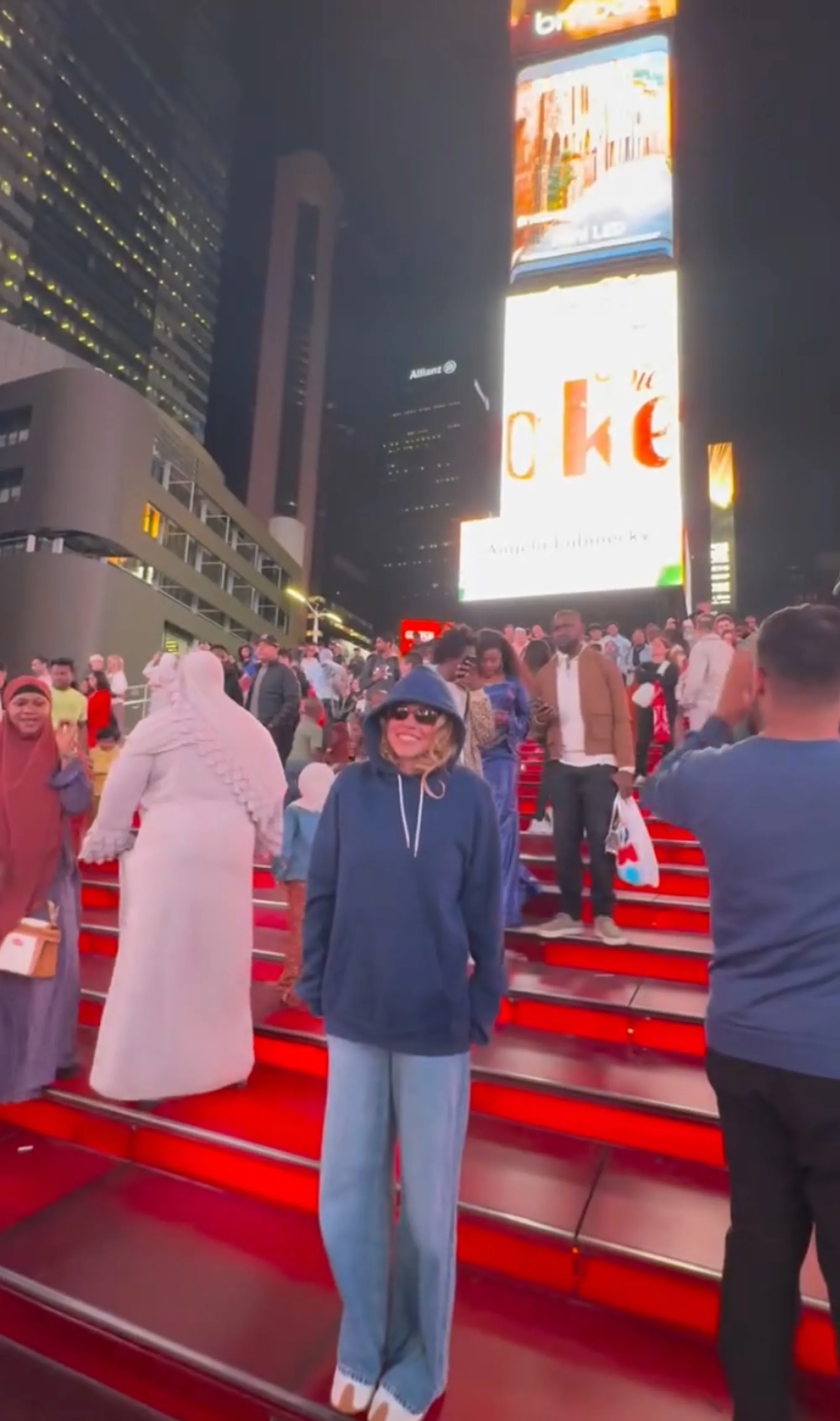 Sydney Sweeney with a person in a navy blue hoodie and sunglasses in Times Square.