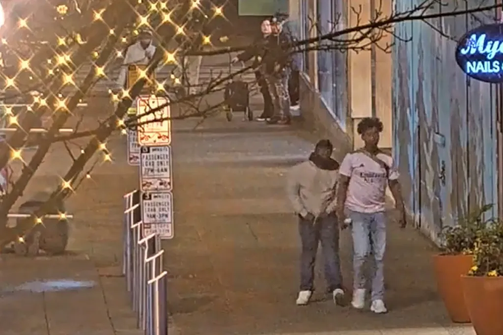 People walking on a city street at night, with a man in a pink shirt and blue jeans in the foreground.