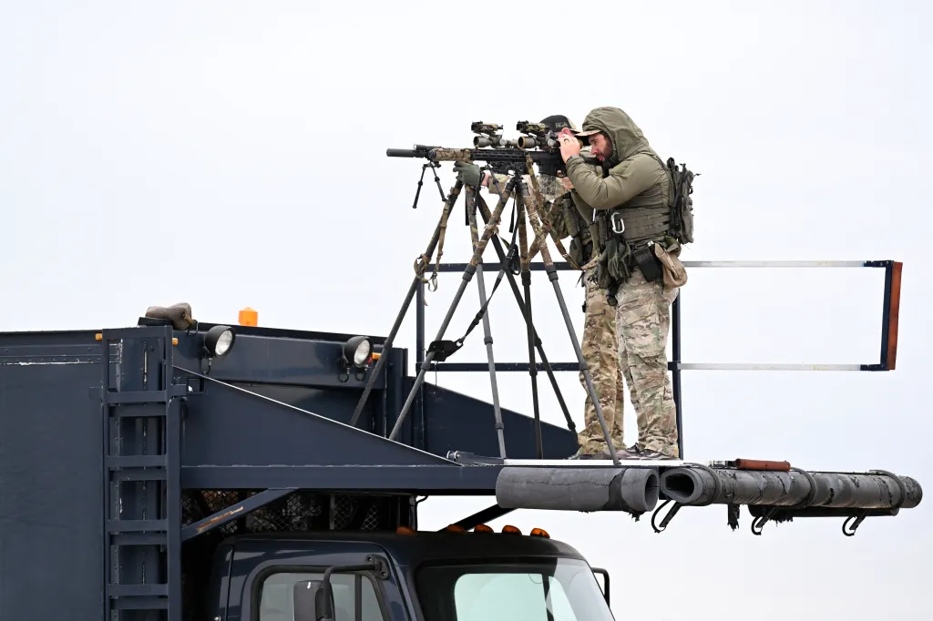 Secret service agents with sniper rifles provide security from a raised platform.