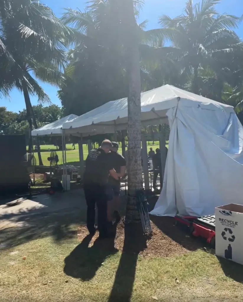 Secret Service agent handcuffing a person near white tents and palm trees.