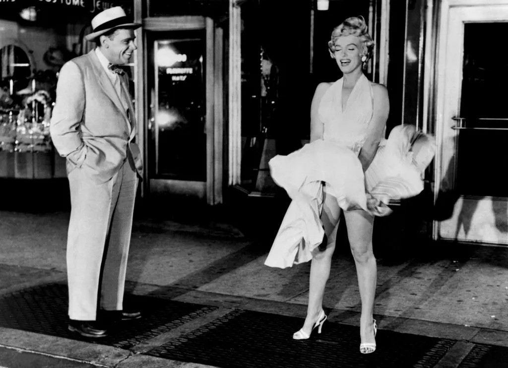 Marilyn Monroe in a white dress over a subway grate, with Tom Ewell watching her.