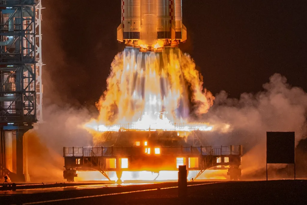 The Shenzhou-23 manned mission launching from the Jiuquan Satellite Launch Center at night, with rocket engines firing.