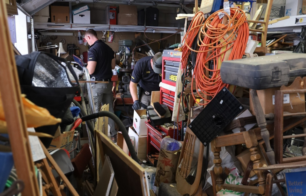 Two investigators searching through a cluttered garage.