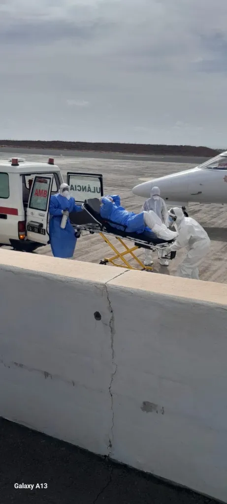Medical workers in PPE transport a patient on a stretcher from an ambulance to a small jet.