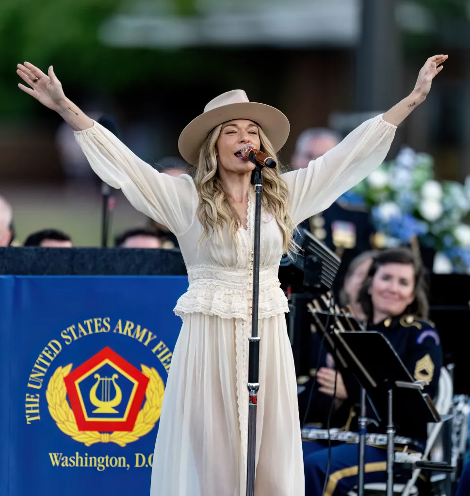 LeAnn Rimes performing in a light-colored dress and hat, with the United States Army Field Band logo visible.