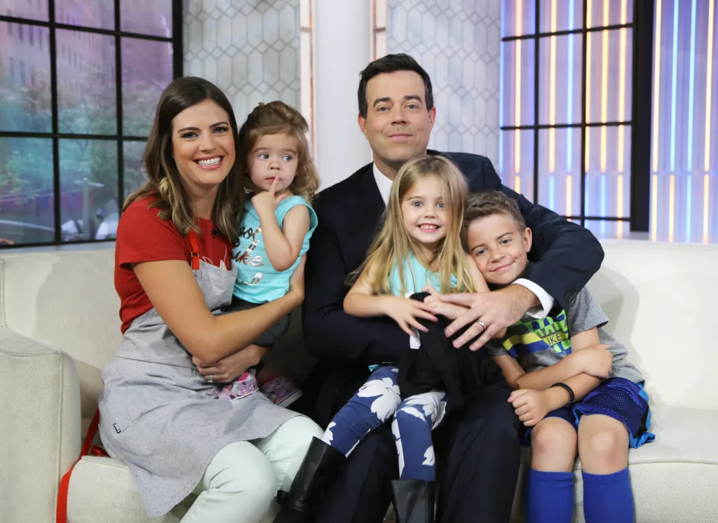 Siri Daly and Carson Daly smiling while holding their children London Rose, Etta Jones, and Jackson James.