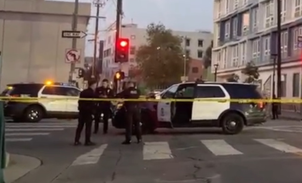 Police officers and patrol cars behind yellow caution tape at the scene of a Skid Row shooting.
