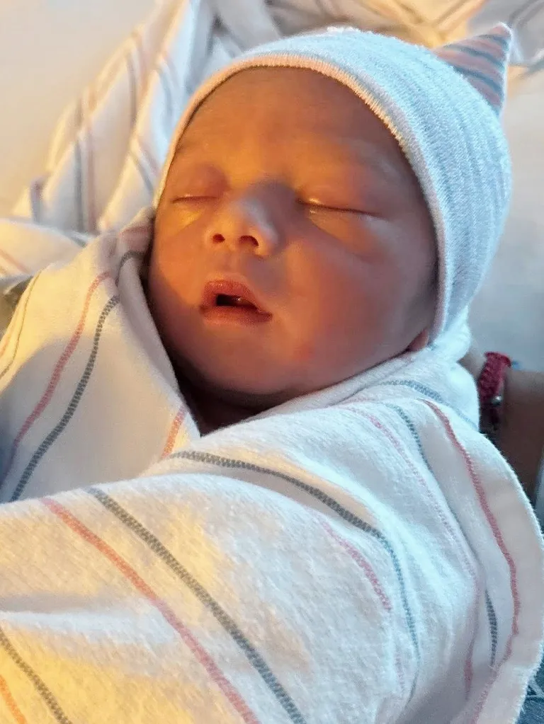 Newborn baby Mateo Gonzalez sleeping, wrapped in a hospital blanket and wearing a striped hat.