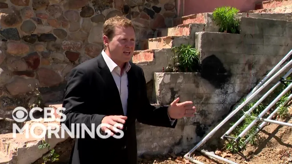 Spencer Pratt in a suit and white shirt, gesturing as he speaks outdoors with stone and concrete structures in the background.