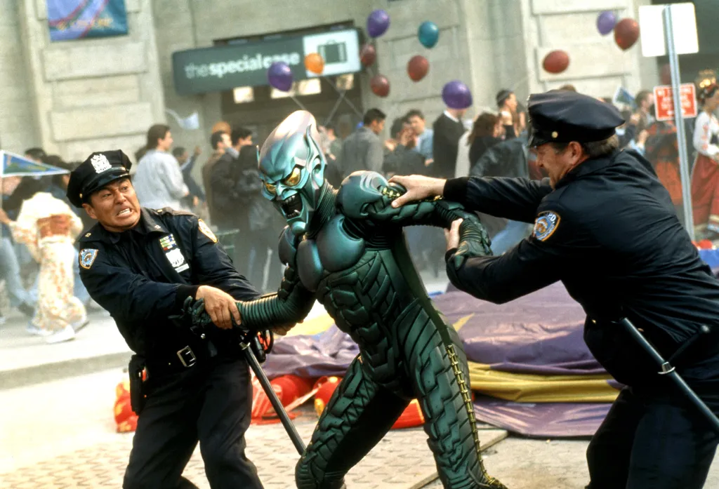 Willem Dafoe as Green Goblin in a green suit struggling against two policemen trying to restrain him.
