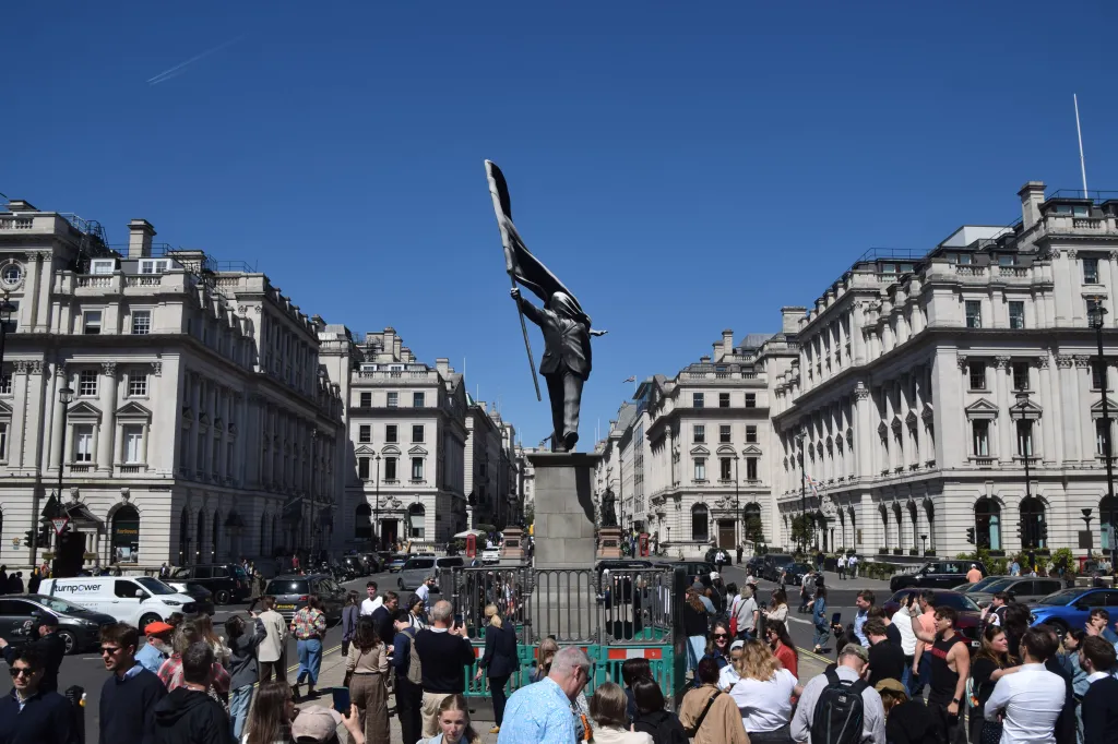 Banksy's newest sculpture in London, showing a person holding a flag that covers their face, surrounded by a crowd of onlookers.
