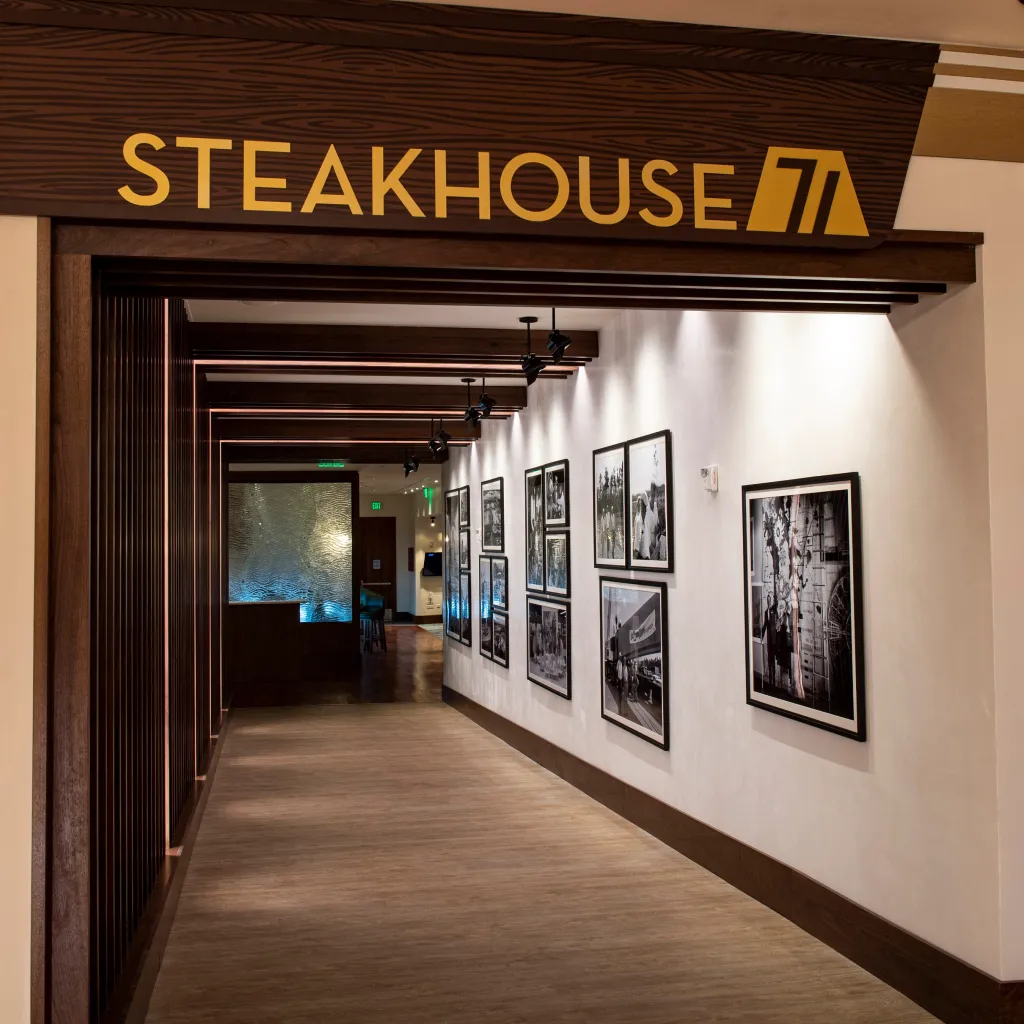 Entrance hallway to Steakhouse 71, with a wooden sign over the doorway, dark wooden accents and light walls, and black-and-white photos displayed on the right.