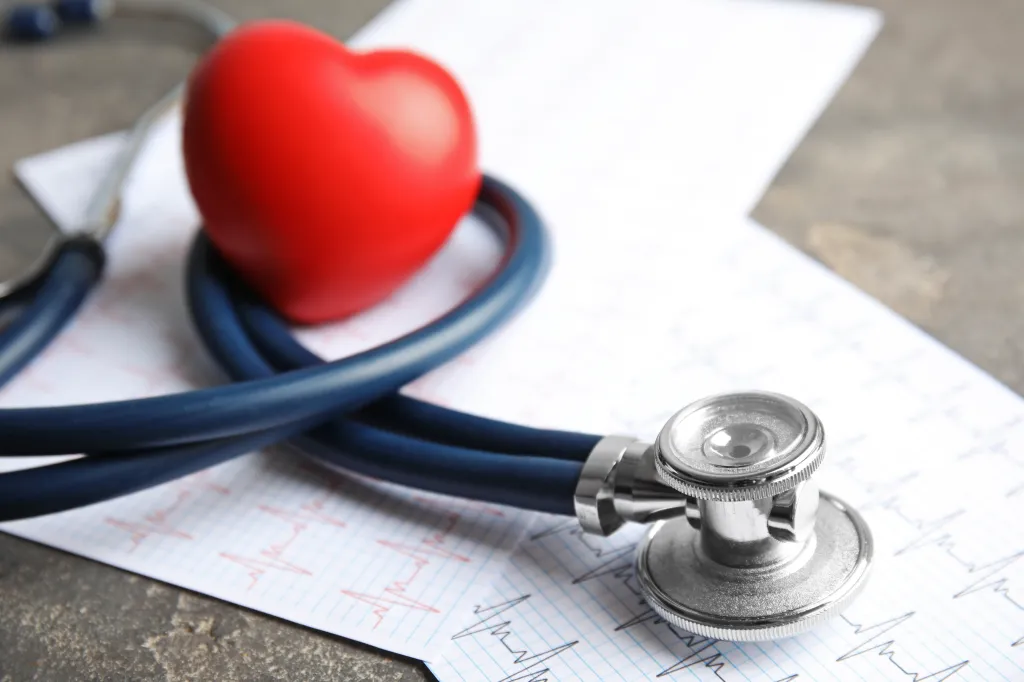 Stethoscope, red heart, and a cardiogram on a gray table.