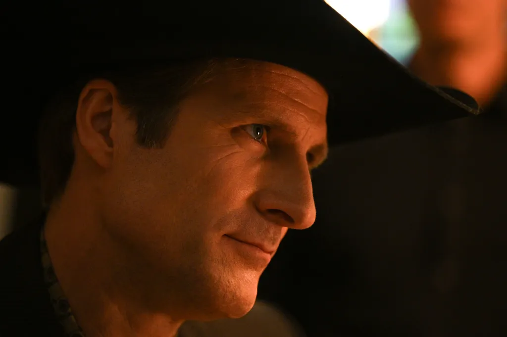 Stew McLean as Hank Riddle in character, wearing a black cowboy hat.