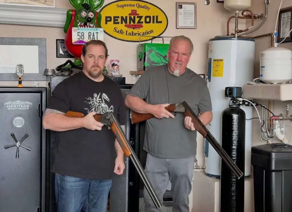 Darrell Sheets and his son Brandon Sheets holding shotguns in front of safes and water heaters.