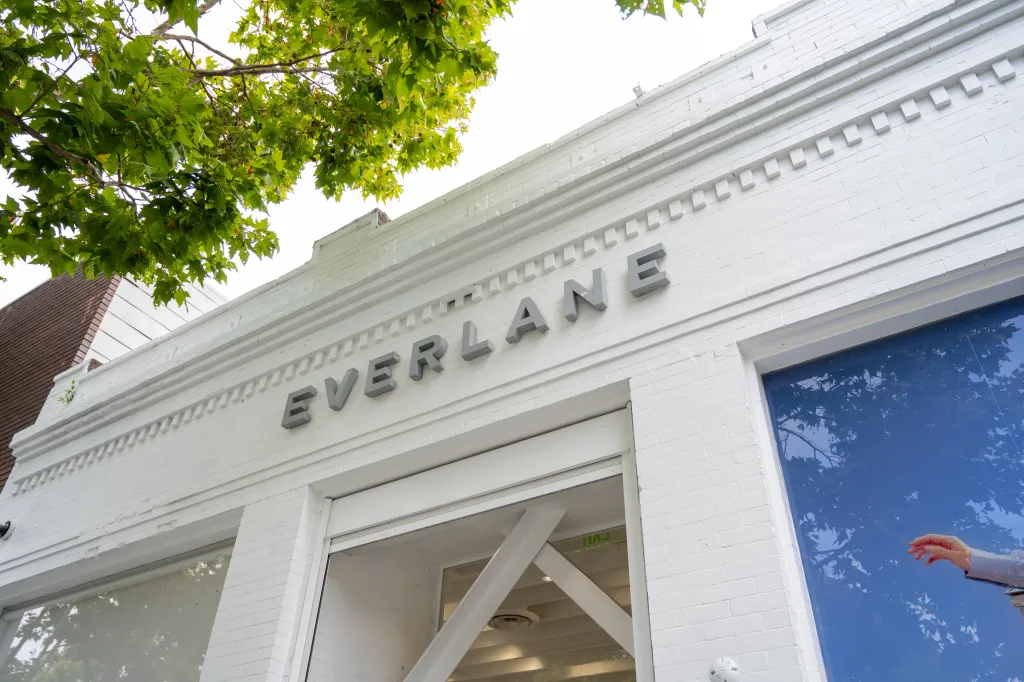 Exterior of Everlane clothing retailer with white brick facade, raised lettering, and leafy tree overhead.