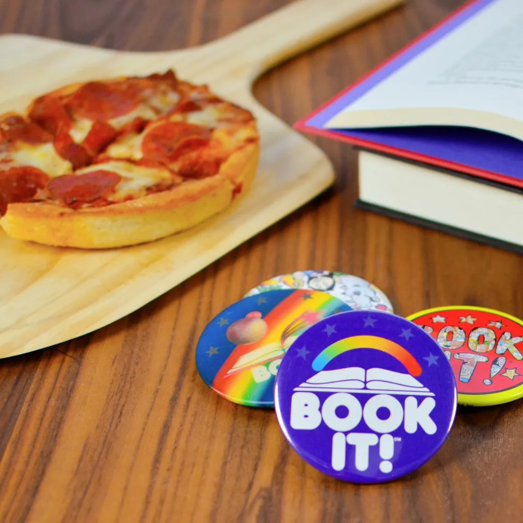 A personal pan pepperoni pizza on a wooden peel next to an open book and three 