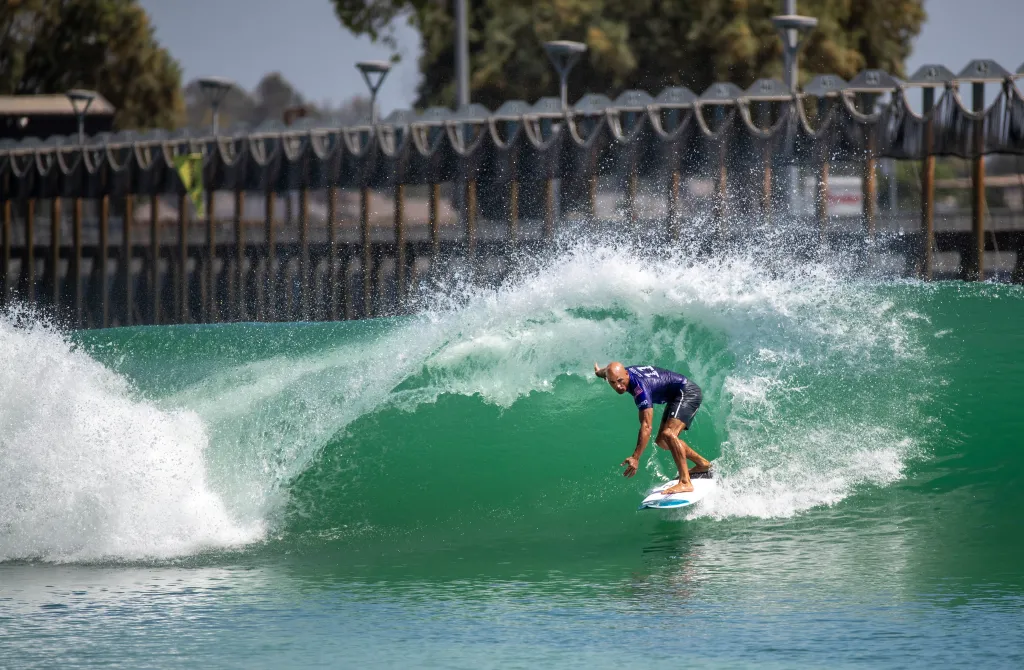 Kelly Slater surfing in a wave pool, turning on a green wave with a white crest.