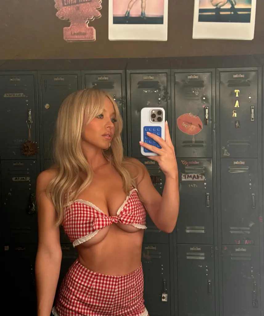 Sydney Sweeney takes a mirror selfie in a red and white gingham outfit in front of lockers.
