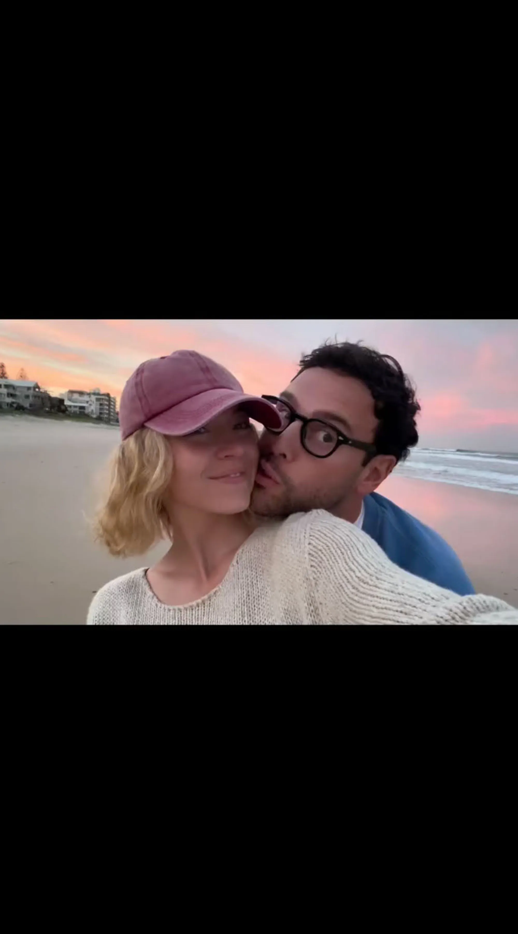 Sydney Sweeney and Scooter Braun posing for a selfie on a beach at sunset, with Braun kissing Sweeney's cheek.