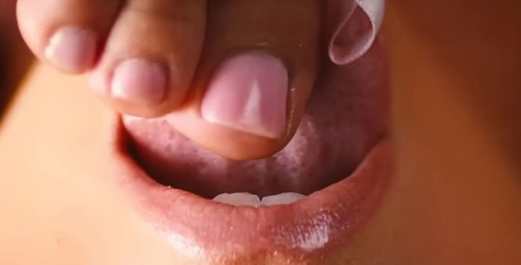 A close-up shot of a manicured finger pressing down on a person's tongue.