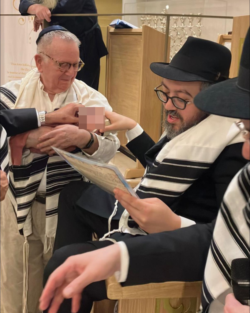 Rabbi Eli Schlanger with a man holding a baby during a religious ceremony.