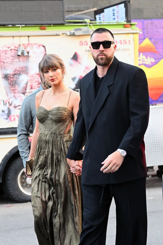 Taylor Swift in a gold gown and Travis Kelce in a dark suit holding hands.