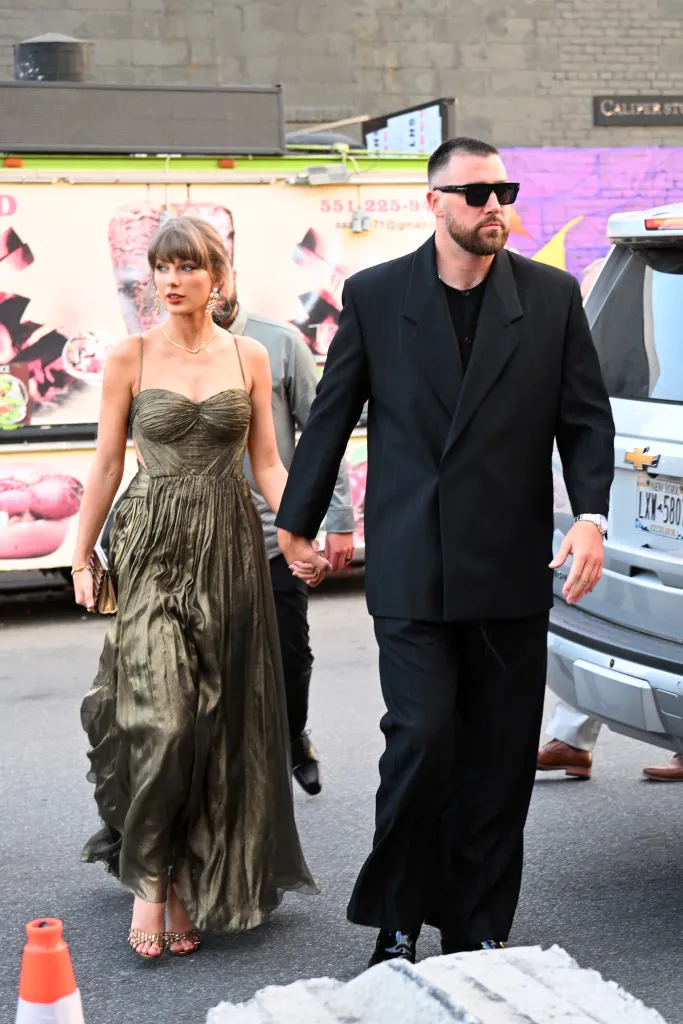 Taylor Swift, in a metallic dress, and Travis Kelce, in a black suit, walking hand-in-hand in New York City.