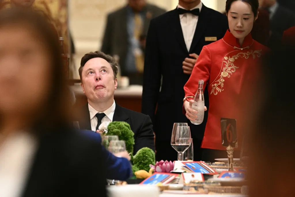Elon Musk looks up during a state banquet in Beijing, with a server in traditional Chinese attire standing nearby.