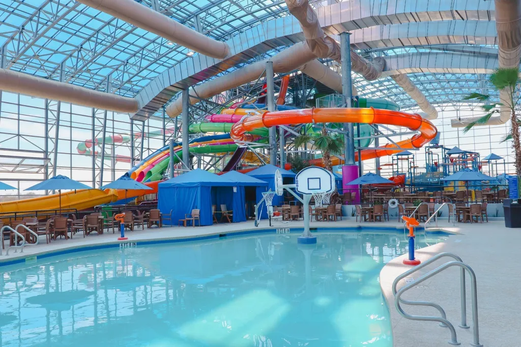 An indoor water park with multiple colorful slides, a pool, and shaded seating areas.