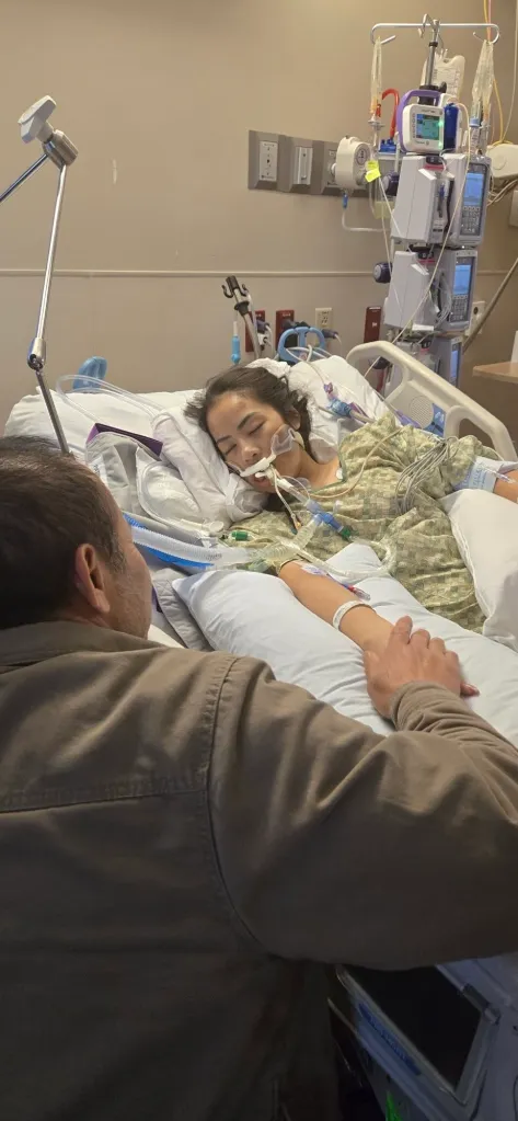 A family member looking over a woman in a hospital bed, who is connected to medical equipment.