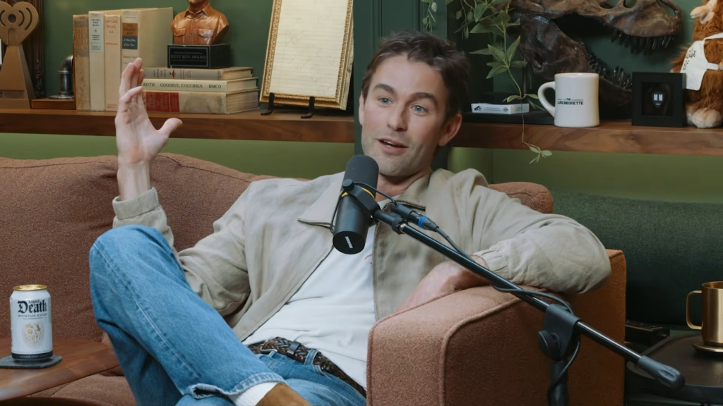 Chace Crawford speaking into a microphone while seated on a couch.