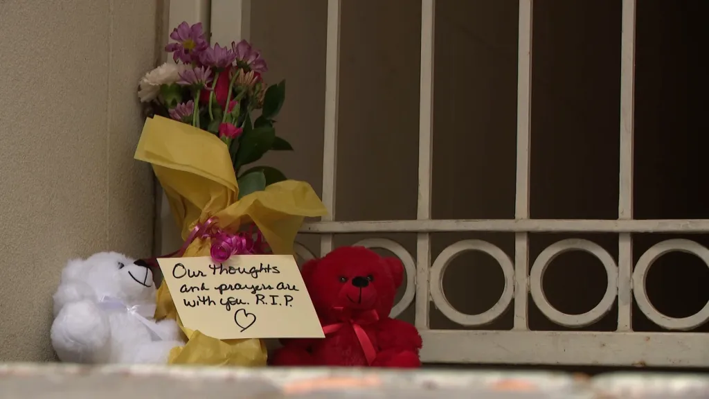 A memorial with flowers, two teddy bears, and a handwritten note that reads, 