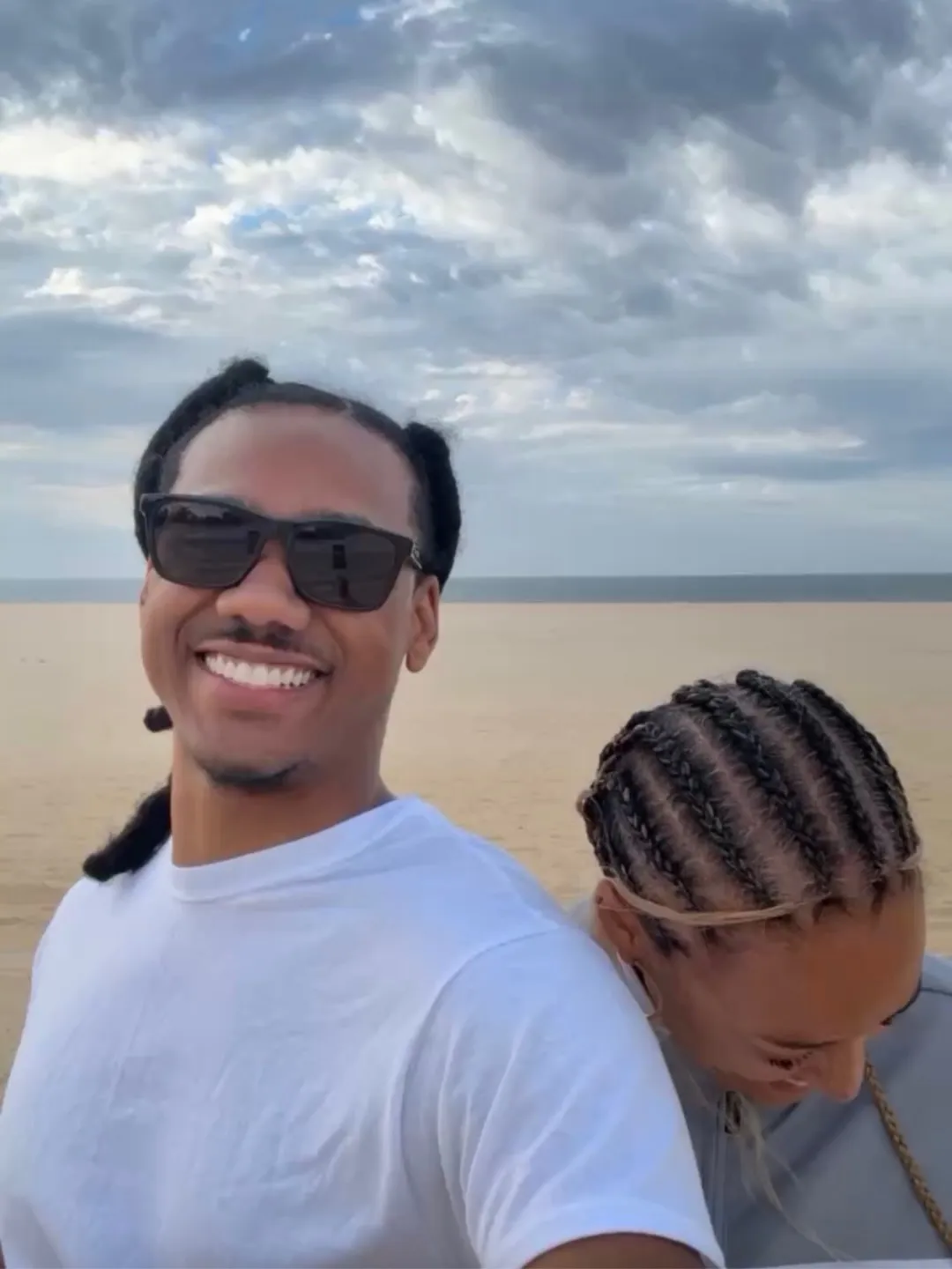Tia Mowry's new boyfriend smiling at the camera with Tia Mowry resting her head on his shoulder on a beach.