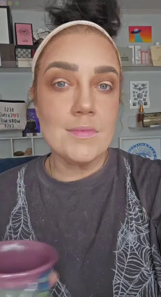 A woman with a white headband and a black shirt with spiderwebs, looking forward.
