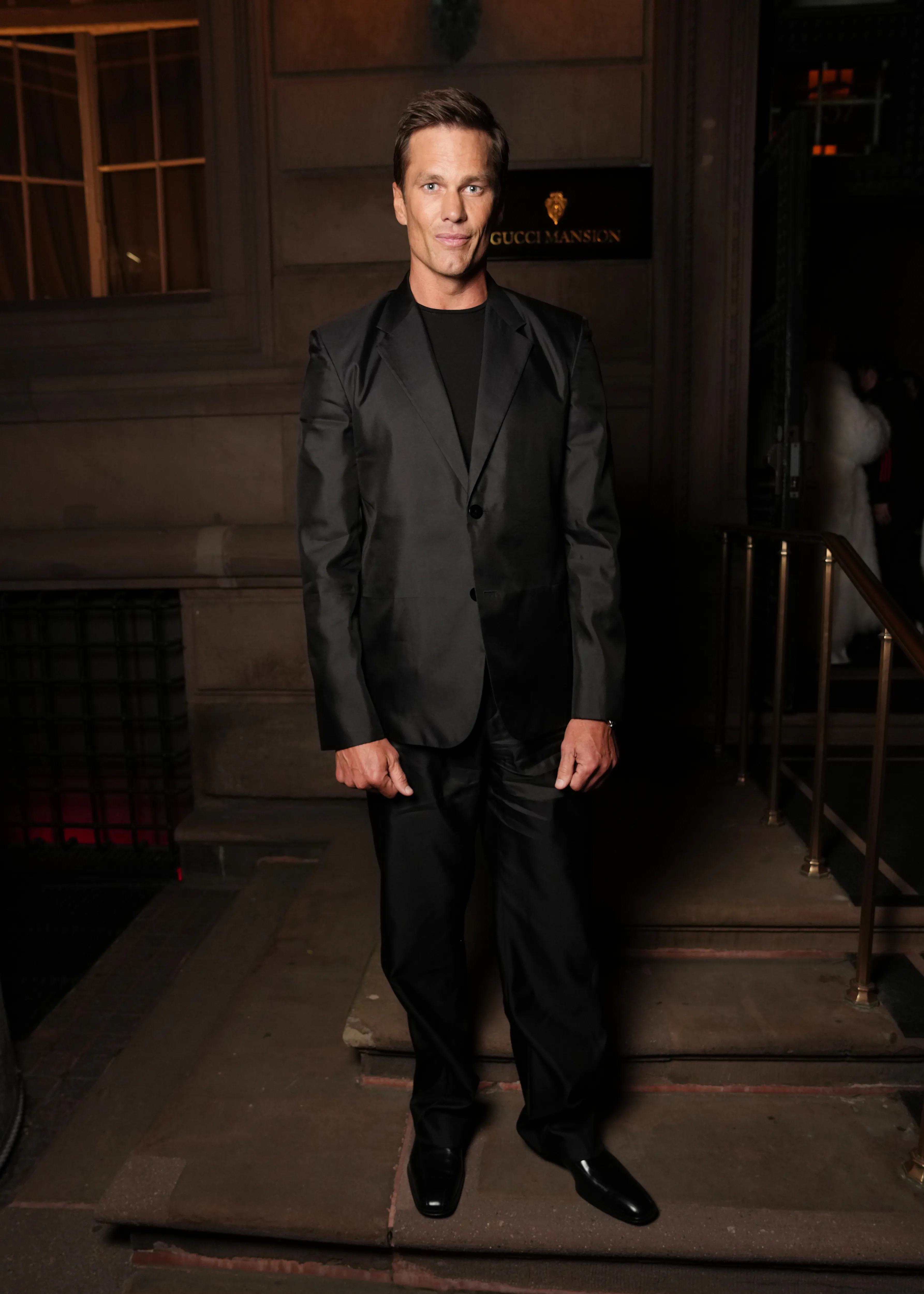 Tom Brady posing in a black suit outside the Gucci Mansion.