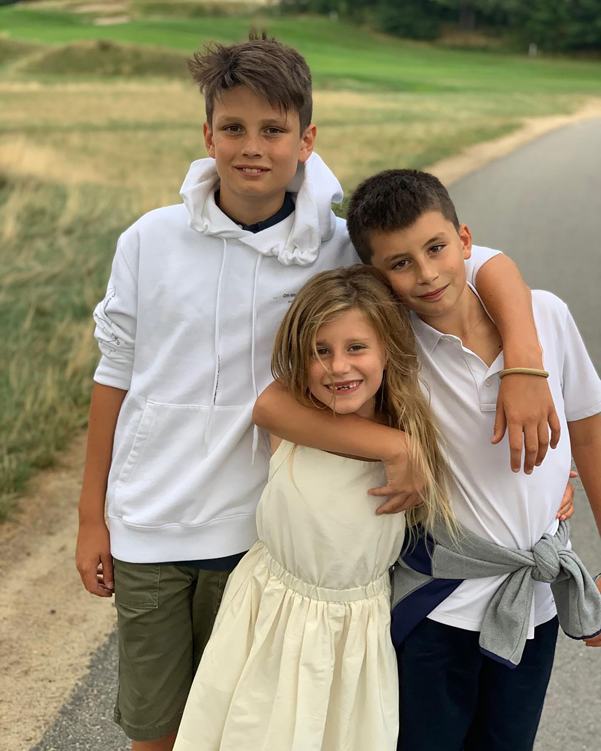 Tom Brady's three children, Jack, Vivian, and Benjamin, standing together outdoors.