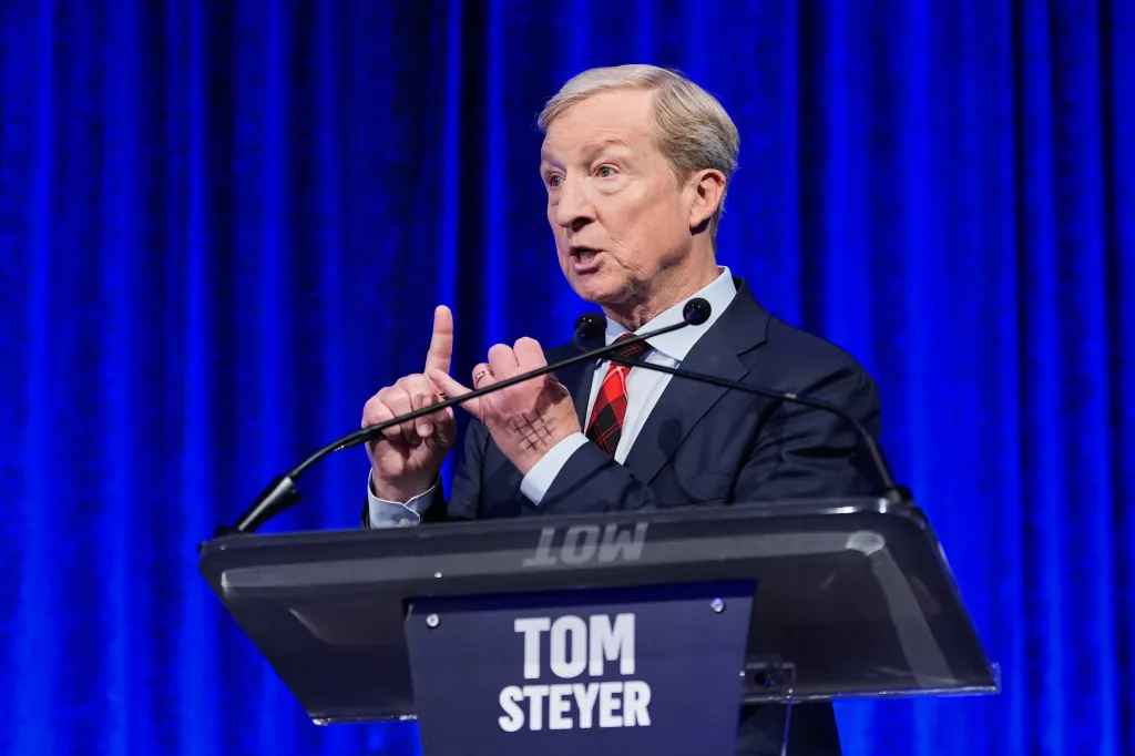 Tom Steyer speaking at a podium with a blue curtain background.