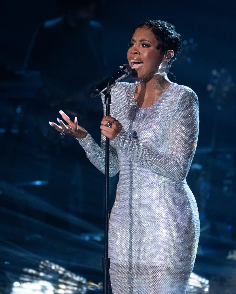 Keyla Richardson singing into a microphone on stage, wearing a shimmering silver dress.