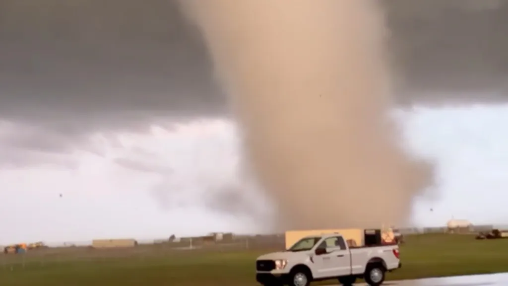 A large tornado sweeps across Vance Air Force Base with a white pickup truck in the foreground.